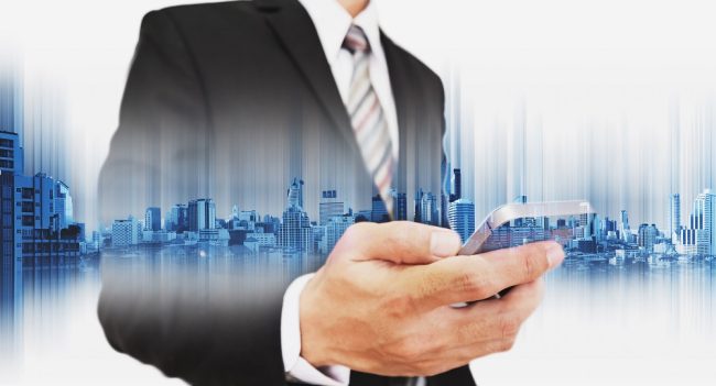 Mężczyzna w garniturze wpatruje się w smartfon, na to nałożona panorama wieżowców nowoczesnego miasta