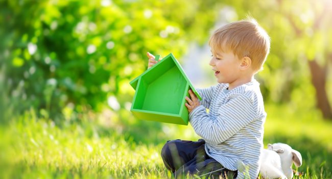 Dziecko siedzi na trawie i trzyma zielony model domu