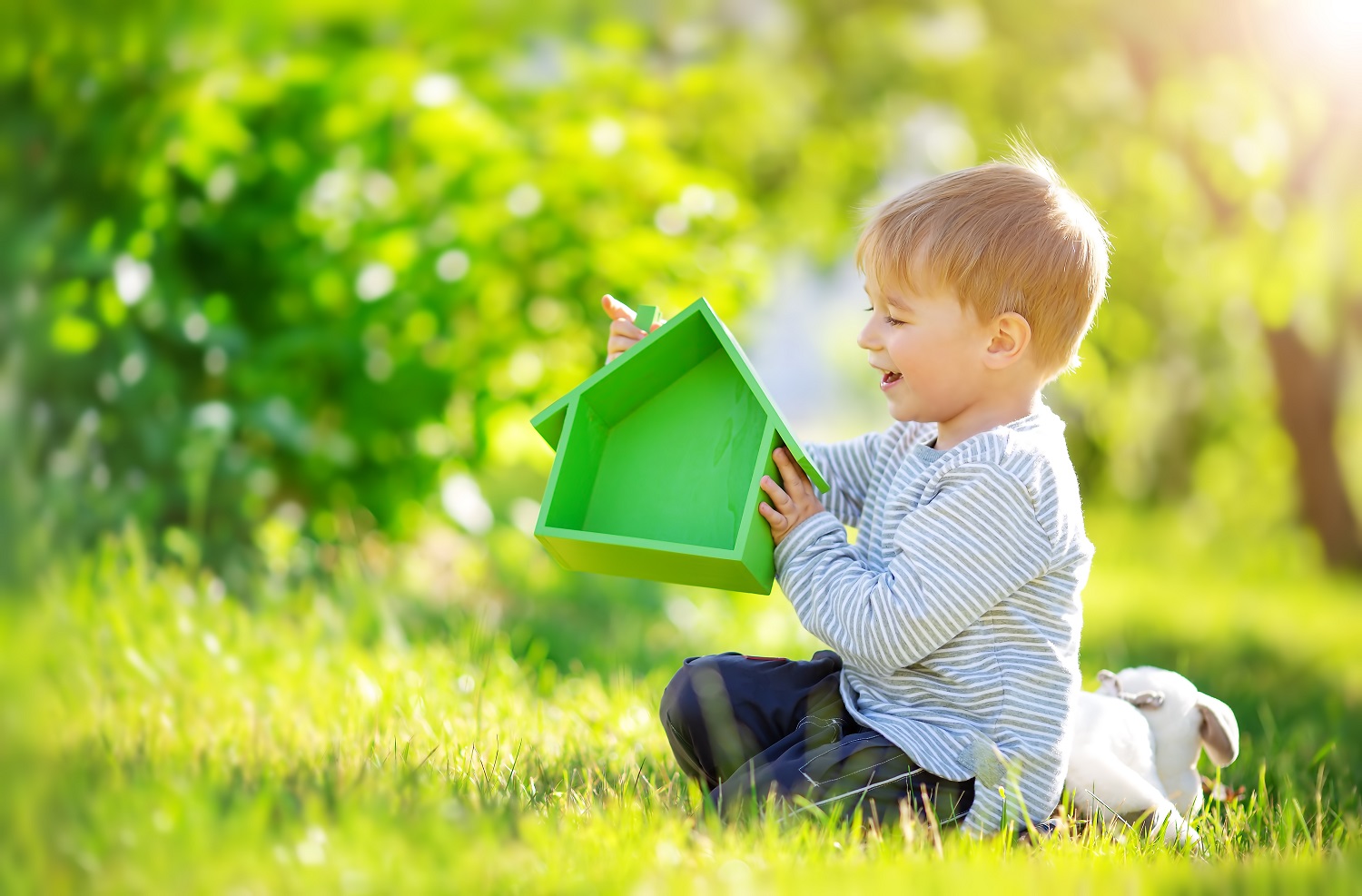 Dziecko siedzi na trawie i trzyma zielony model domu